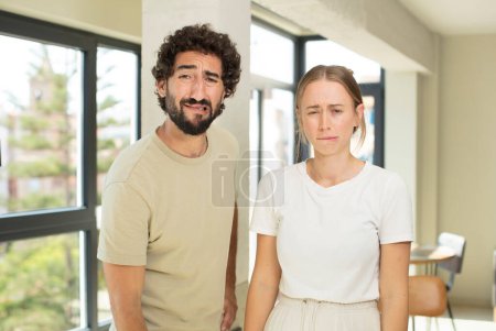 Foto de Joven pareja adulta sintiéndose triste y quejumbrosa con una mirada infeliz, llorando con una actitud negativa y frustrada - Imagen libre de derechos