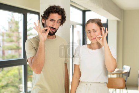 Photo for Young adult couple looking serious and displeased with both fingers crossed up front in rejection, asking for silence - Royalty Free Image