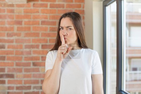 Foto de Young adult pretty woman looking serious and cross with finger pressed to lips demanding silence or quiet, keeping a secret - Imagen libre de derechos