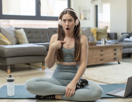 Photo for Young adult woman practicing yoga looking shocked and surprised with mouth wide open, pointing to self - Royalty Free Image