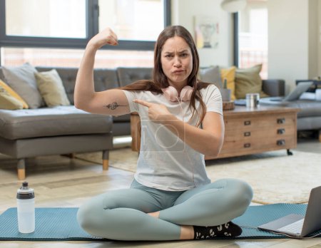 Téléchargez les photos : Jeune femme adulte pratiquant le yoga se sentant heureuse, satisfaite et puissante, flexion ajustement et biceps musculaires, regardant fort après la salle de gym - en image libre de droit