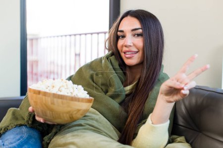 Téléchargez les photos : Young pretty woman eating popcorns sitting on a couch at home - en image libre de droit