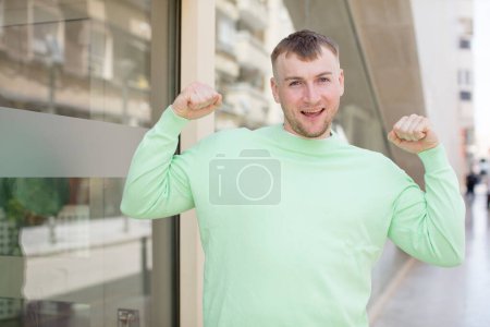 Téléchargez les photos : Bel homme se sentant heureux, satisfait et puissant, flexion ajustement et biceps musculaires, regardant fort après la salle de gym - en image libre de droit