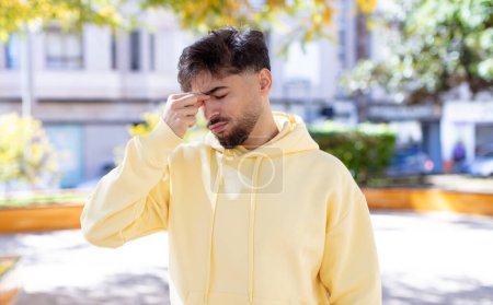 Téléchargez les photos : Jeune homme beau se sentant stressé, malheureux et frustré, touchant le front et souffrant de migraine de maux de tête graves - en image libre de droit