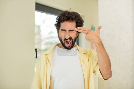 Photo for Young crazy bearded man looking unhappy and stressed, suicide gesture making gun sign with hand, pointing to head - Royalty Free Image