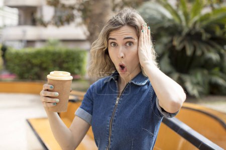 Foto de Pretty woman feeling extremely shocked and surprised. take away coffee concept - Imagen libre de derechos