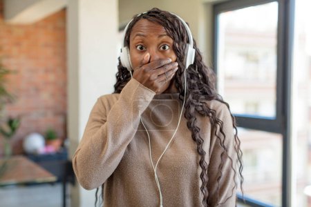 Téléchargez les photos : Afro femme noire couvrant la bouche avec une main et une expression choquée ou surprise. concept de musique d'écoute - en image libre de droit