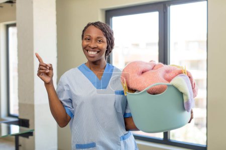 Foto de Negro afro mujer sonriendo alegremente, sintiéndose feliz y señalando hacia un lado. concepto de lavandería y limpieza - Imagen libre de derechos
