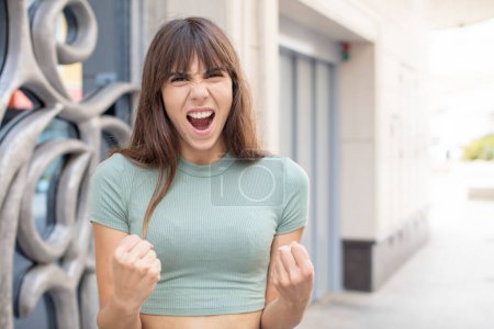 Photo for Pretty young woman shouting aggressively with annoyed, frustrated, angry look and tight fists, feeling furious - Royalty Free Image
