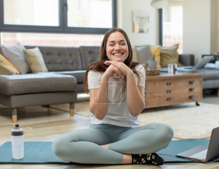 Téléchargez les photos : Jeune femme adulte pratiquant le yoga heureux et excité, surpris et étonné, gloussant avec une expression mignonne - en image libre de droit
