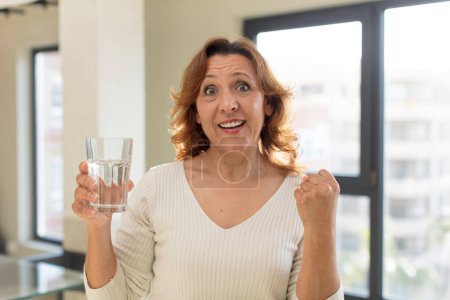 Photo for Middle age pretty woman feeling shocked,laughing and celebrating success. water glass - Royalty Free Image