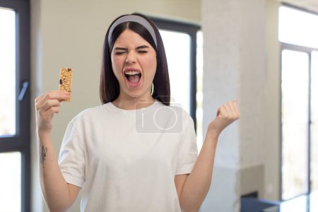 Foto de Mujer joven bonita mirando enojado, molesto y frustrado. concepto de barra de cereal fitness - Imagen libre de derechos