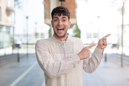 Photo for Young handsome man smiling cheerfully and pointing to copy space on palm on the side, showing or advertising an object - Royalty Free Image