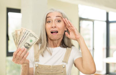 Foto de Mujer bastante mayor mirando feliz, asombrado y sorprendido. con billetes en dólares - Imagen libre de derechos