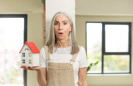 Photo for Pretty senior woman feeling extremely shocked and surprised. with a house model - Royalty Free Image