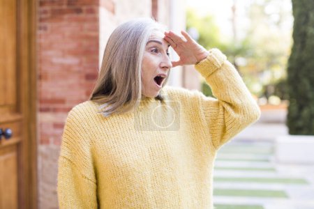 Photo for Senior retired pretty white hair woman looking bewildered and astonished, with hand over forehead looking far away, watching or searching - Royalty Free Image