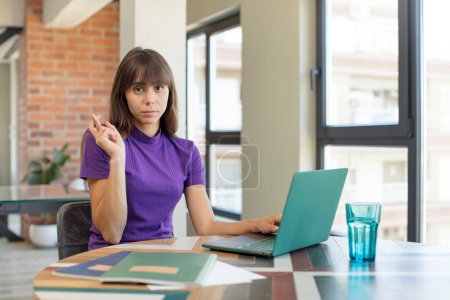 Photo for Young pretty woman crossing fingers and hoping for good luck.  universitary student with a laptop - Royalty Free Image