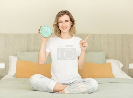 Photo for Pretty woman smiling cheerfully, feeling happy and pointing to the side alarm clock concept - Royalty Free Image