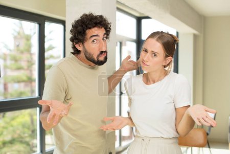 Foto de Young adult couple feeling clueless and confused, having no idea, absolutely puzzled with a dumb or foolish look - Imagen libre de derechos