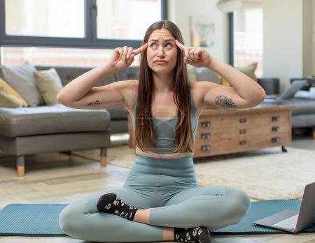 Photo for Young adult woman practicing yoga feeling confused or doubting, concentrating on an idea, looking to copy space on side - Royalty Free Image