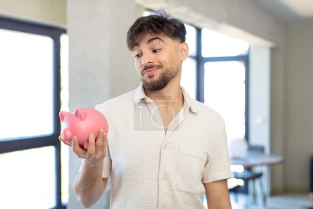 Photo for Young handsome man smiling and looking with a happy confident expression. piggy bank concept - Royalty Free Image