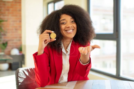 Foto de Mujer negra bastante afro sonriendo felizmente y ofreciendo o mostrando un concepto. concepto de moneda virtual - Imagen libre de derechos