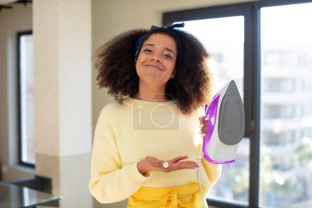 Photo for Pretty afro black woman smiling cheerfully, feeling happy and showing a concept. iron clothes laundry concept - Royalty Free Image