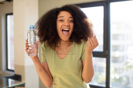 Téléchargez les photos : Jolie afro femme noire se sentant choquée, riant et célébrant le succès. concept de bouteille d'eau - en image libre de droit