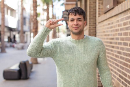 Foto de Joven hombre guapo sosteniendo un objeto, mostrando, ofreciendo o anunciando algo pequeño - Imagen libre de derechos