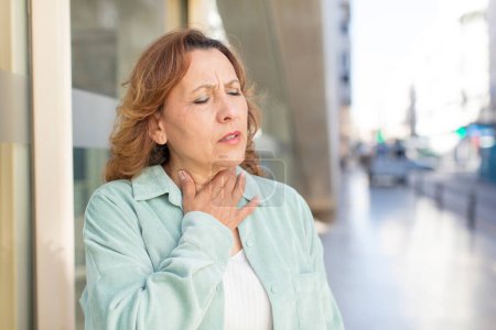 Téléchargez les photos : Femme d'âge moyen se sentant malade avec un mal de gorge et des symptômes de grippe, toux avec la bouche couverte - en image libre de droit