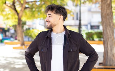 Photo for Young handsome man looking happy, cheerful and confident, smiling proudly and looking to side with both hands on hips - Royalty Free Image