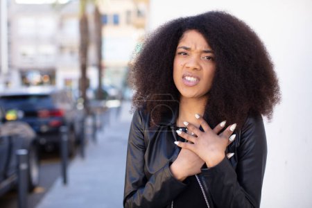 Foto de Mujer bonita afroamericana que se ve triste, herida y con el corazón roto, sosteniendo ambas manos cerca del corazón, llorando y sintiéndose deprimida - Imagen libre de derechos