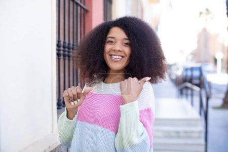 Photo for African american pretty woman smiling cheerfully and casually pointing to copy space on the side, feeling happy and satisfied - Royalty Free Image