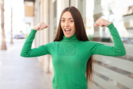 Photo for Young pretty woman feeling happy, satisfied and powerful, flexing fit and muscular biceps, looking strong after the gym - Royalty Free Image