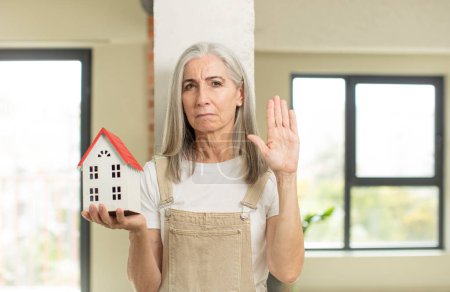 Photo for Pretty senior woman looking serious showing open palm making stop gesture. with a house model - Royalty Free Image