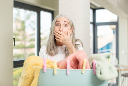 Photo for Pretty senior woman covering mouth with a hand and shocked or surprised expression. washing clothes concept - Royalty Free Image