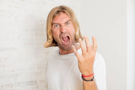Photo for Young blond adult man looking angry, annoyed and frustrated screaming wtf or whats wrong with you - Royalty Free Image