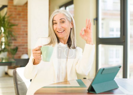 Téléchargez les photos : Senior jolie femme se sentant heureux, montrant l'approbation avec un geste correct avec un écran tactile - en image libre de droit