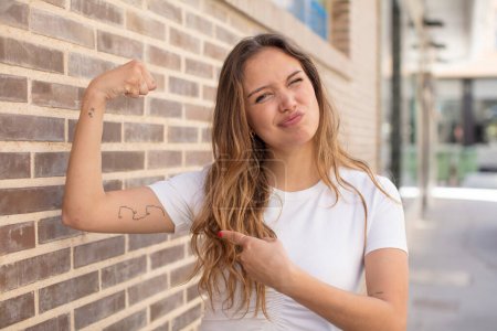 Photo for Pretty hispanic woman feeling happy, satisfied and powerful, flexing fit and muscular biceps, looking strong after the gym - Royalty Free Image