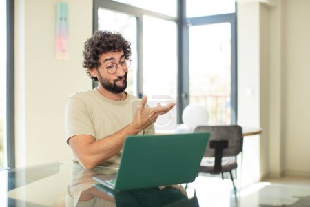 Foto de Joven hombre barbudo adulto con un ordenador portátil sentirse confundido y despistado, preguntándose acerca de una explicación dudosa o pensamiento - Imagen libre de derechos