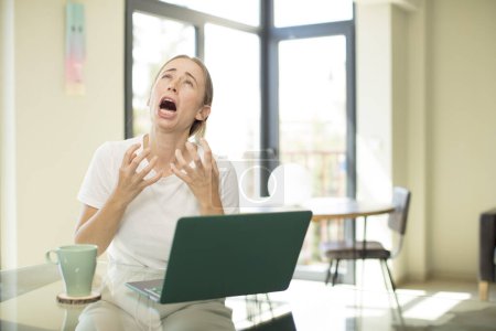 Foto de Mujer guapa caucásica con un ordenador portátil que parece desesperado y frustrado, estresado, infeliz y molesto, gritando y gritando - Imagen libre de derechos