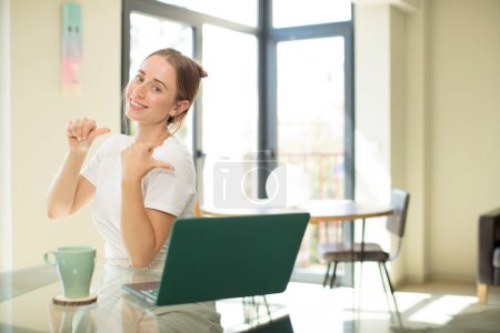 Téléchargez les photos : Caucasienne jolie femme avec un ordinateur portable souriant joyeusement et occasionnellement pointant pour copier l'espace sur le côté, se sentant heureux et satisfait - en image libre de droit