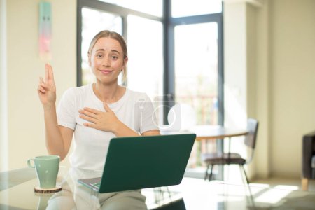 Photo for Caucasian pretty woman with a laptop looking happy, confident and trustworthy, smiling and showing victory sign, with a positive attitude - Royalty Free Image