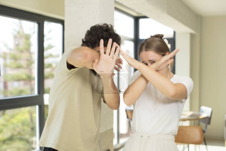 Photo for Young adult couple covering face with hand and putting other hand up front to stop camera, refusing photos or pictures - Royalty Free Image