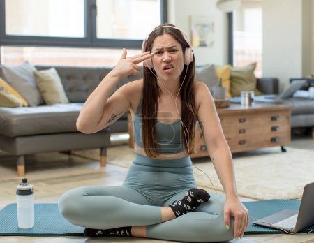 Foto de Mujer adulta joven que practica yoga que mira infeliz y estresado, gesto suicida que hace la muestra del arma con la mano, señalando a la cabeza - Imagen libre de derechos