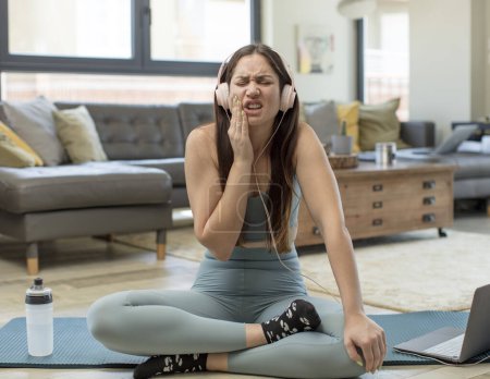 Téléchargez les photos : Jeune femme adulte pratiquant le yoga tenant la joue et souffrant de maux de dents douloureux, se sentant malade, malheureux et malheureux, à la recherche d'un dentiste - en image libre de droit