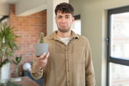 Photo for Young handsome man feeling sad and whiney with an unhappy look and crying. cactus plant concept - Royalty Free Image