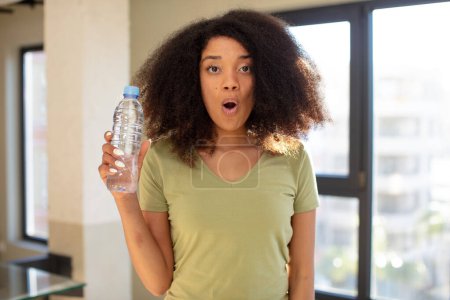 Téléchargez les photos : Jolie afro femme noire se sentant extrêmement choqué et surpris. concept de bouteille d'eau - en image libre de droit