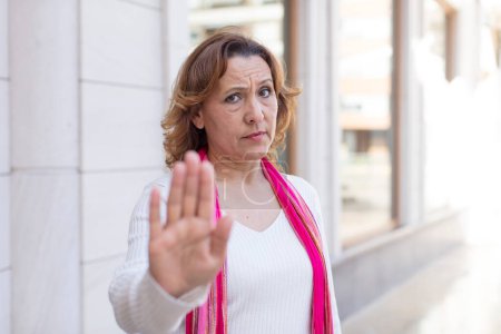 Photo for Middle age woman looking serious, stern, displeased and angry showing open palm making stop gesture - Royalty Free Image