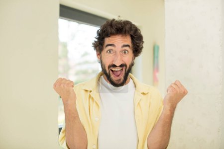Téléchargez les photos : Jeune homme barbu fou se sentant choqué, excité et heureux, rire et célébrer le succès, dire wow! - en image libre de droit